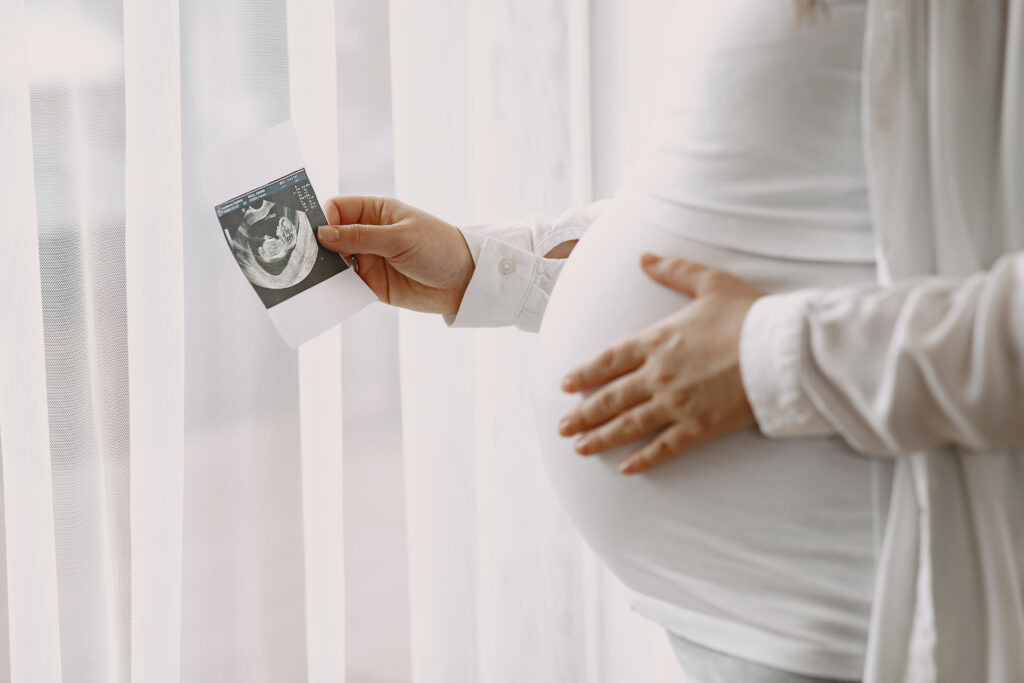 Woman standing by the window. Pregnant looking at photo. Woman expecting a baby. Журналист