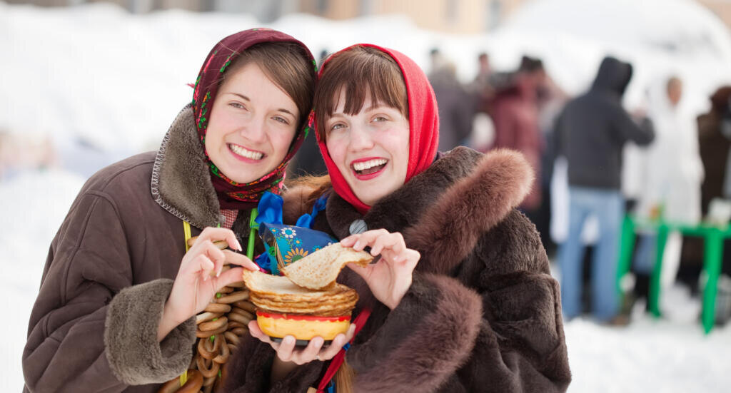Girls in traditional clothes tasting pancake during Shrovetide Журналист