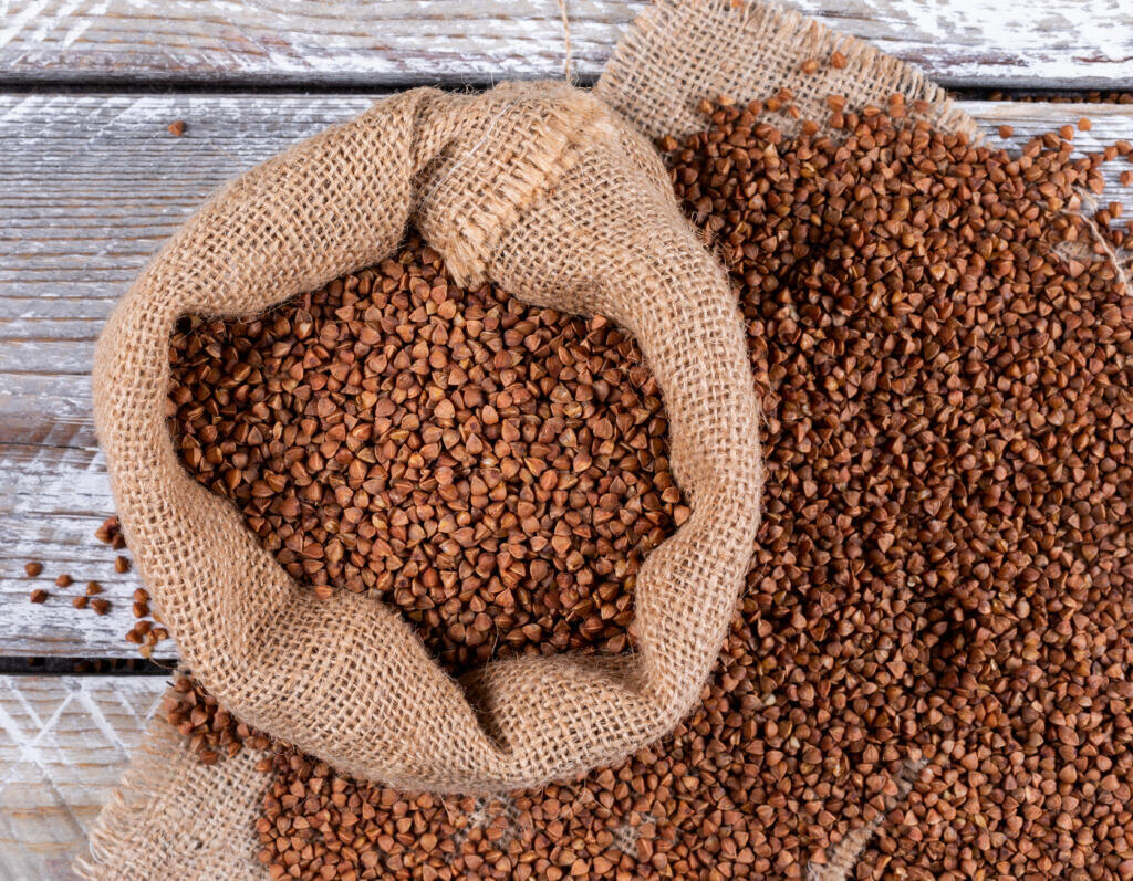 Buckwheats in a sack on a sack cloth and light wooden background. flat lay. Журналист