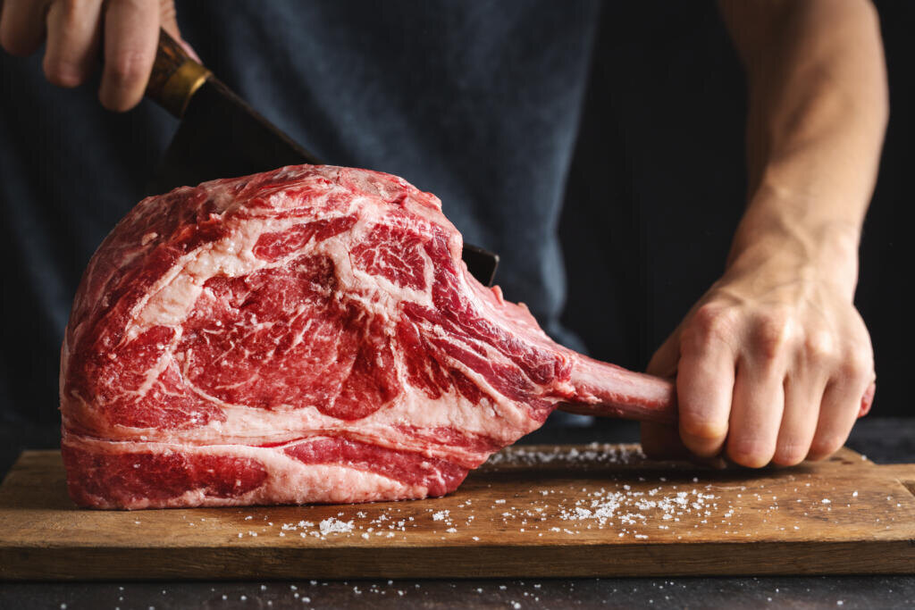 Butcher cuting fresh appetizing tomahawk steak on old wooden board. Closeup Журналист