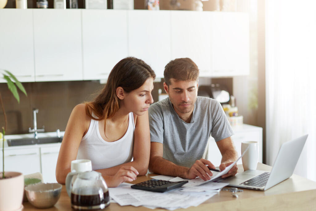 Portrait of serious man and female sitting at kitchen table, dealing with financial issues, holding documents. Family couple calculating their debts while sitting together at kitchen. Business concept Журналист