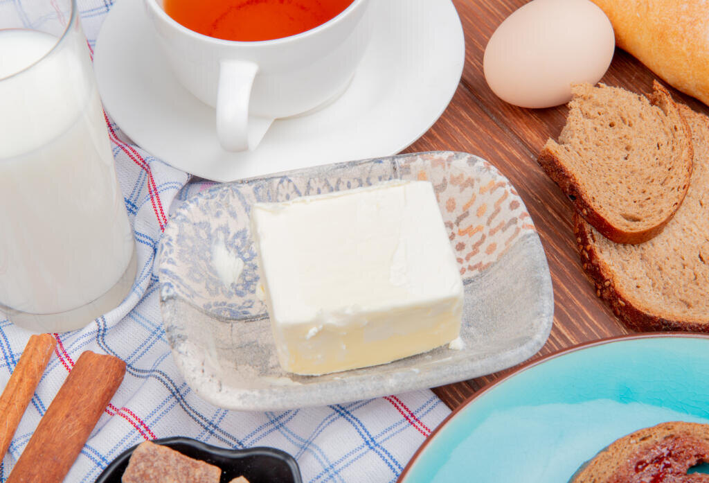 side view of breakfast set with butter rye bread slices smeared with jam in plate milk cinnamon tea on plaid cloth and wooden background Журналист