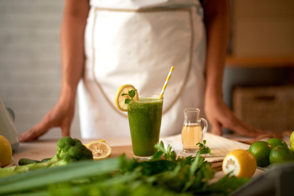 Glass of green smoothie on table in front of woman sho made it Журналист
