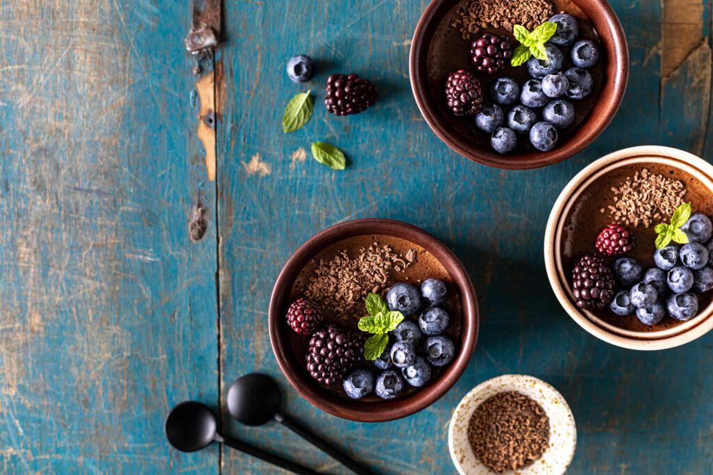 Chocolate mousse with blueberries and blackberries and fresh mint in ramekins on a blue wooden table. Top view with a place to copy. Журналист