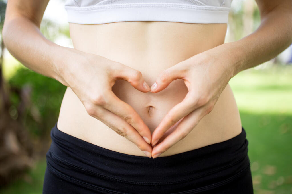Close-up of female hands shaping heart on belly outdoors. Fitness and dieting concept Журналист