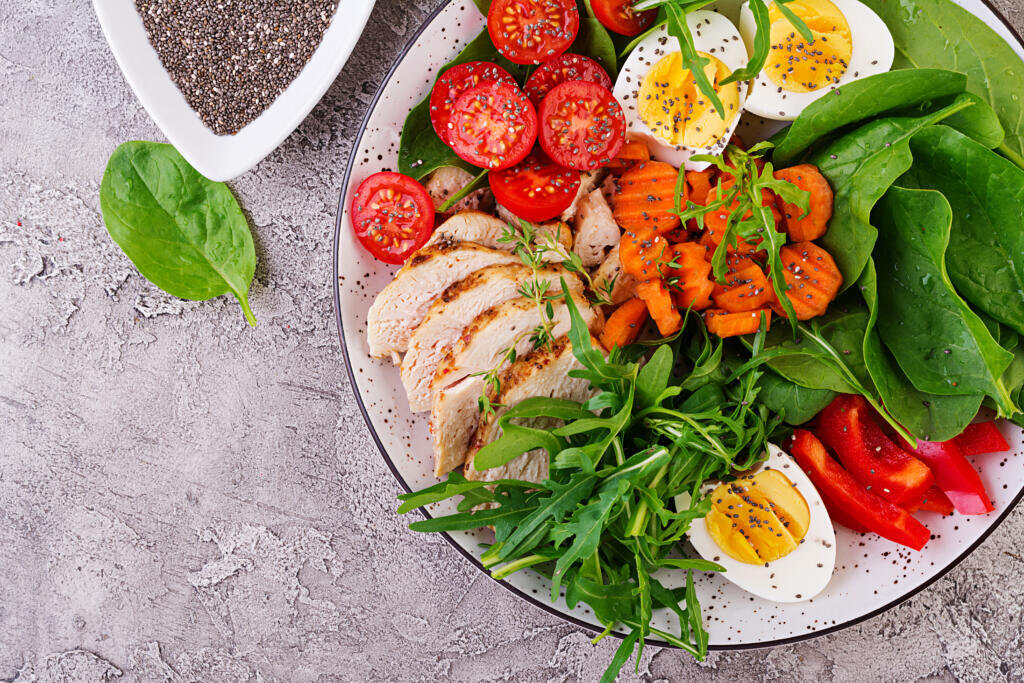 Plate with a keto diet food. Cherry tomatoes, chicken breast, eggs, carrot, salad with arugula and spinach. Keto lunch. Top view Журналист