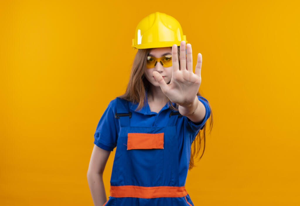 young woman builder worker in construction uniform and safety helmet standing with open hand making stop sign Журналист