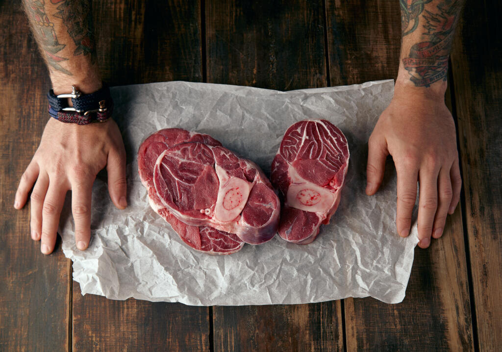 Top view of two tattooed hands and three steaks on white craft paper on old wooden table Журналист