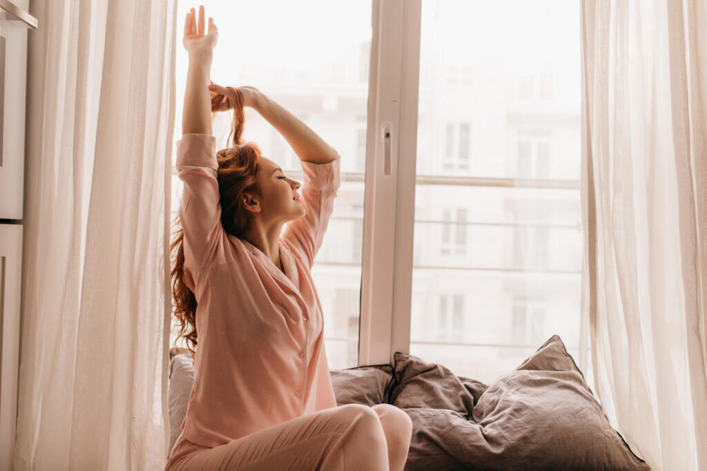 Cute female model in pink pajama enjoying morning. Pleasant ginger woman sitting on bed. Журналист